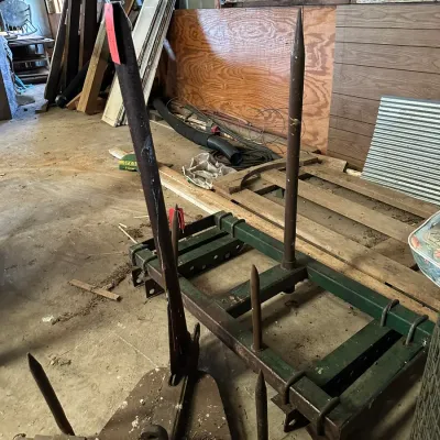 Sale Photo Thumbnail #209: Heavy-duty 3-point hitch round bale spear attachment along with an additional farm implement frame in a workshop setting.