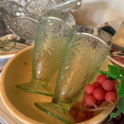 Sale Photo Thumbnail #673: Pair of green Depression glass footed tumblers with floral embossments, sitting inside a yellow ceramic mixing bowl.