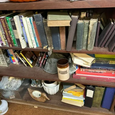 Sale Photo Thumbnail #309: Wooden bookcase filled with vintage books, DVDs, a stoneware utensil crock, binders, and miscellaneous household items.