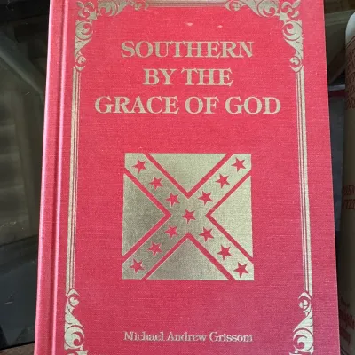 Sale Photo Thumbnail #419: Hardcover copy of "Southern By The Grace of God" by Michael Andrew Grissom, featuring a red cloth cover with gilt lettering and border detailing.