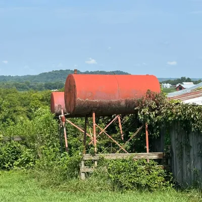 Sale Photo Thumbnail #755: Two elevated vintage red metal fuel tanks supported by metal frames, showing weather wear and surface rust.