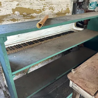 Sale Photo Thumbnail #467: Vintage painted wooden structure repurposed into a display shelf featuring an integrated set of piano-style keys. The piece shows heavy distressing, worn green paint, and weathered wood surfaces.