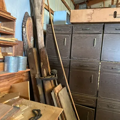 Sale Photo Thumbnail #513: Workshop featuring stacked dark faux-wood cabinets, assorted reclaimed lumber, live-edge wood slabs, and vintage tools.