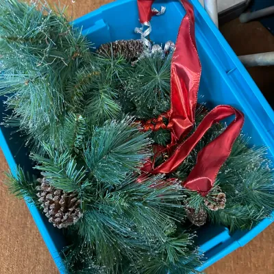 Sale Photo Thumbnail #76: Blue plastic storage bin filled with artificial frosted pine garland, pinecones, and red ribbon.