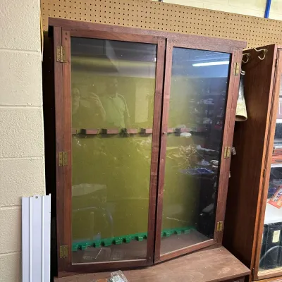 Sale Photo Thumbnail #320: Wooden dual glass-door gun cabinet with brass hardware, featuring interior barrel racks and felt lining over a lower drawer base.
