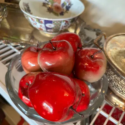 Sale Photo Thumbnail #678: Clear glass bowl filled with glossy artificial red apples, displayed alongside vintage porcelain and silverplate serving pieces.