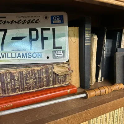 Sale Photo Thumbnail #59: Wooden bookshelf displaying antique religious books, a small branding iron with a turned wood handle, and a 2009 Williamson County, Tennessee license plate.