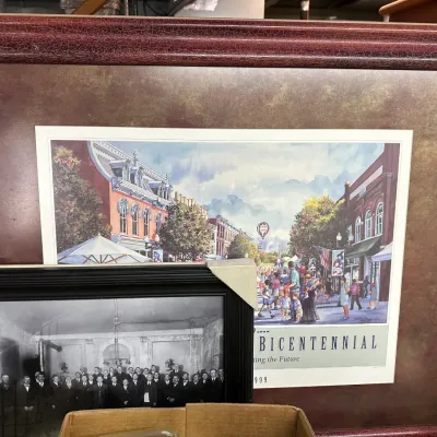 Sale Photo Thumbnail #11: Large framed Bicentennial print with a crackle-finish reddish wood frame, displayed alongside a smaller framed black and white photograph.