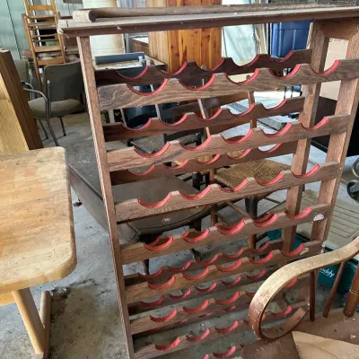 Sale Photo Thumbnail #735: Large free-standing wooden wine rack with red felt lining along the scalloped bottle slots, displayed among other vintage furniture in a storage space.