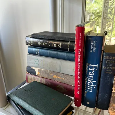 Sale Photo Thumbnail #261: Assortment of vintage hardback books, including religious texts and reference volumes, arranged on a white wire shelf.