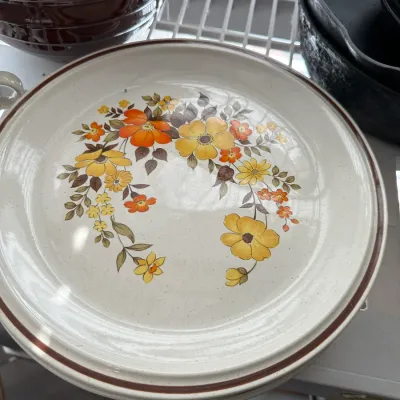 Sale Photo Thumbnail #693: Vintage stoneware dinnerware featuring a 1970s floral pattern in orange and yellow tones with brown accent trim.