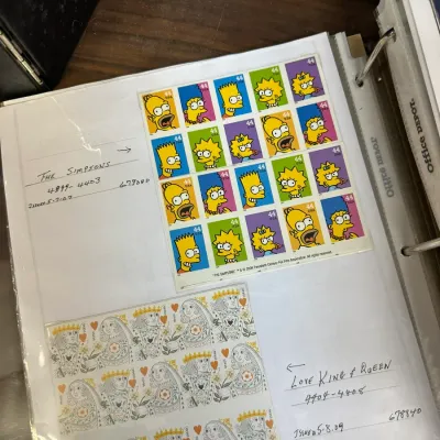 Sale Photo Thumbnail #110: A page in a stamp collector binder featuring a sheet of 2009 USPS 44-cent The Simpsons postage stamps and Love King & Queen stamps.