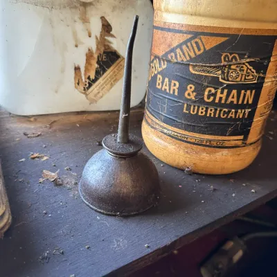 Sale Photo Thumbnail #489: Vintage metal thumb-pump oil can displayed alongside a bottle of Gold Band bar and chain lubricant and a plastic fluid jug.