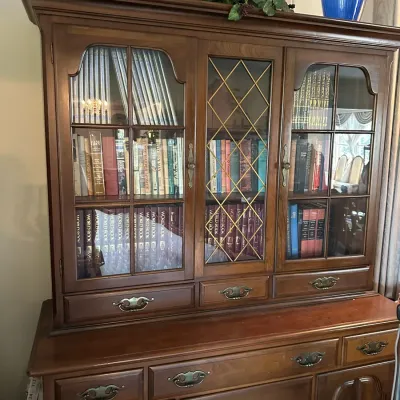 Sale Photo Thumbnail #643: Traditional wooden hutch cabinet featuring glass-front display doors and lower storage drawers, filled with books.