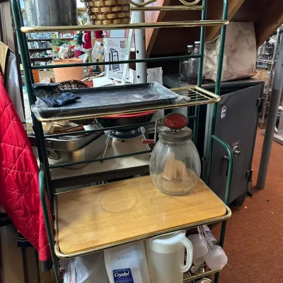 Sale Photo Thumbnail #91: Vintage green and brass metal baker's rack holding various household items, including a clear glass butter churn and kitchenware.