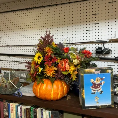 Sale Photo Thumbnail #310: Autumn floral arrangement in a faux pumpkin planter, alongside a boxed Holiday Time decoration, illuminated miniature house, and fishing rods mounted on a pegboard.