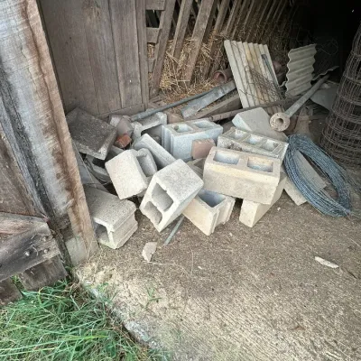 Sale Photo Thumbnail #330: Pile of concrete cinder blocks, metal pipe scrap, and rolls of wire fence stored inside a wooden barn structure.