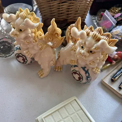 Sale Photo Thumbnail #410: Pair of carved faux ivory or resin Chinese foo dog figurines resting on embroidered or decorated balls.