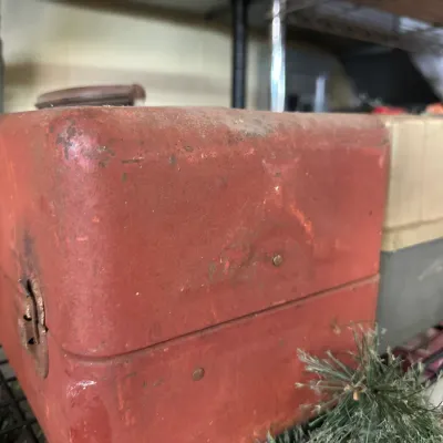 Sale Photo Thumbnail #79: Vintage red metal tackle box or tool chest showing age-appropriate wear and patina, displayed on a wire shelf alongside a plastic storage container.