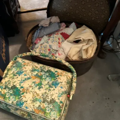 Sale Photo Thumbnail #369: Vintage floral print train case sewing basket alongside a large open round hat box filled with sorted textiles.