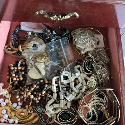 Sale Photo Thumbnail #141: Open jewelry box drawer filled with an assortment of vintage costume jewelry, including beaded necklaces, silver-tone cuffs, gold-tone chain links, and a snowman pendant.
