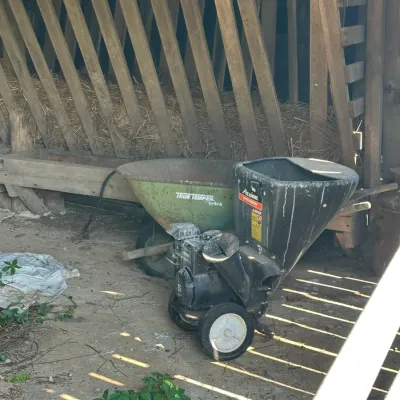 Sale Photo Thumbnail #757: Gas-powered Action wood chipper shredder and a green True Temper wheelbarrow stored in a barn.