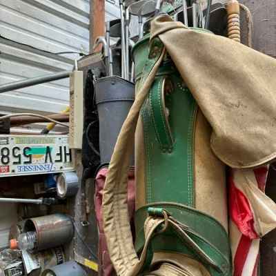Sale Photo Thumbnail #730: Vintage green and tan canvas golf bag packed with various irons and woods, showing signs of heavy wear.