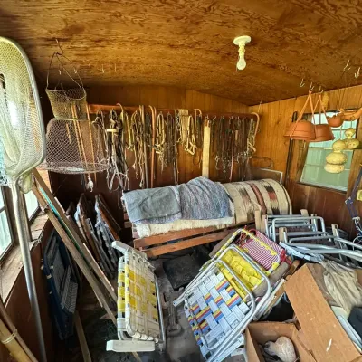 Sale Photo Thumbnail #271: Collection of vintage outdoor gear including aluminum webbed lawn chairs, fishing nets, horse tack, and textiles inside a wood-paneled shed.