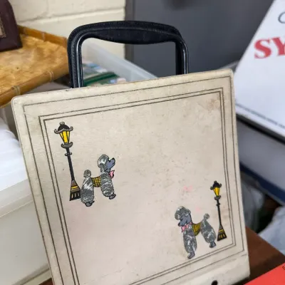 Sale Photo Thumbnail #121: Vintage 1950s vinyl photo album with a black plastic handle, featuring a streetlamp and poodle motif on the off-white cover.