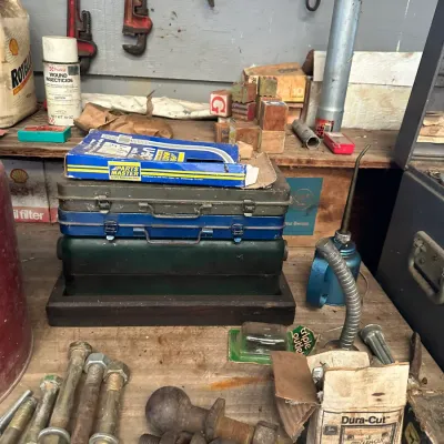 Sale Photo Thumbnail #481: Workbench organized with vintage toolboxes, various hardware including large bolts and hitch balls, an oil can, and automotive supplies.