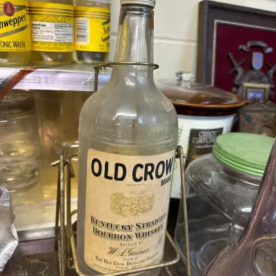 Sale Photo Thumbnail #32: Vintage Old Crow Brand Kentucky Straight Bourbon Whiskey clear glass bottle resting in a brass cradle dispenser.