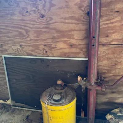 Sale Photo Thumbnail #575: Vintage yellow Shell oil drum can showing heavy patina, surface rust, and wear, positioned in a storage area.