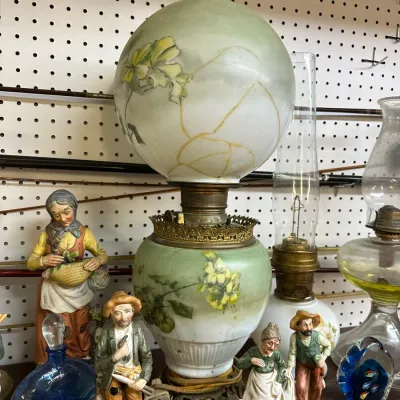 Sale Photo Thumbnail #44: Vintage Gone with the Wind style oil lamp featuring hand-painted floral details on soft green glass, shown with visible cracking on the globe alongside small porcelain figurines.