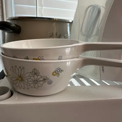 Sale Photo Thumbnail #690: Pair of vintage Corning Ware 'Meadow' pattern saucepan bowls with integrated handles, displayed alongside other kitchen cookware.