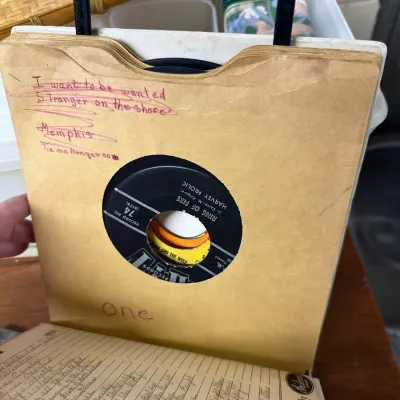 Sale Photo Thumbnail #122: Vintage 45 RPM record tote case containing vinyl singles in handwritten paper sleeves, featuring tracks like Johnny Cash's 'Ring of Fire'.