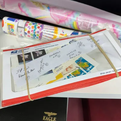 Sale Photo Thumbnail #114: Collection of vintage postage stamp sheets packaged in a USPS Priority Mail envelope, shown alongside rolls of gift wrapping paper.