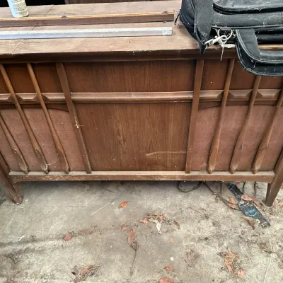 Sale Photo Thumbnail #532: Mid-century modern walnut stereo console featuring decorative carved wooden accents over speaker mesh panels, showing visible wear and dust.