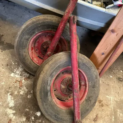 Sale Photo Thumbnail #207: Pair of vintage boat launcher wheels with attached red metal tubular frame components, showing wear and paint loss.