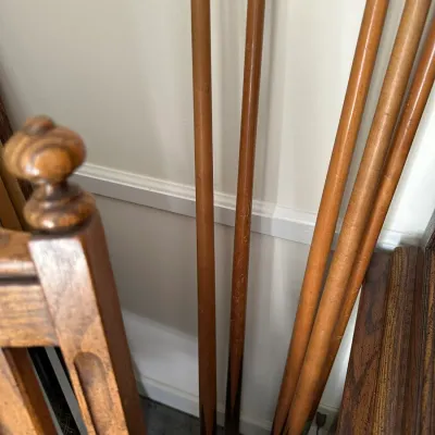 Sale Photo Thumbnail #378: Collection of traditional wooden pool cues leaning against a wall, showing light finish wear from age and use.