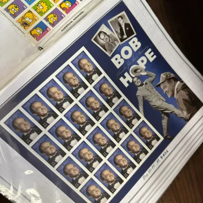 Sale Photo Thumbnail #111: A 2009 USPS Bob Hope commemorative 44-cent stamp pane, displayed in a binder page alongside a sheet of The Simpsons postage stamps.