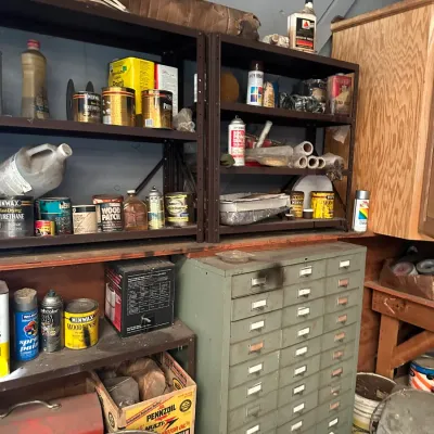 Sale Photo Thumbnail #496: Vintage olive green metal multi-drawer parts cabinet alongside metal shelving units filled with various paints, stains, and automotive chemicals.