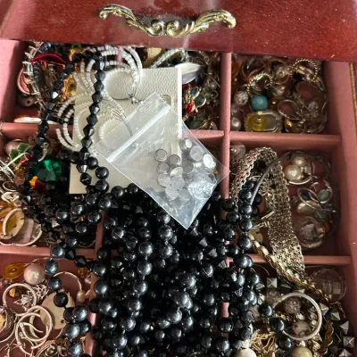 Sale Photo Thumbnail #142: Jewelry box drawer filled with an assortment of costume jewelry, including black beaded necklaces, clip-on and hoop earrings, and various chains.