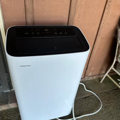 Sale Photo Thumbnail #187: Toshiba portable air conditioner unit in modern white and black, complete with power cord.