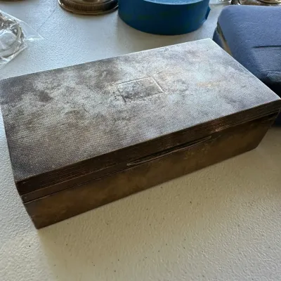 Sale Photo Thumbnail #395: Vintage tarnished silver-plated rectangular keepsake box with textured lid detailing, shown among various estate table items.