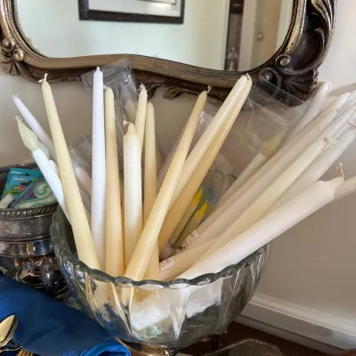 Sale Photo Thumbnail #670: Large collection of white and cream taper candles housed in a scalloped clear glass pedestal bowl.