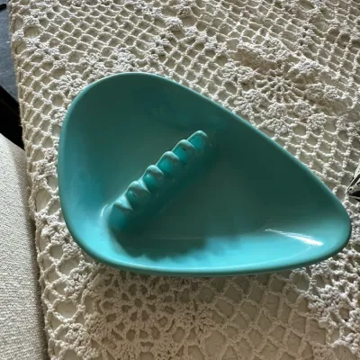 Sale Photo Thumbnail #600: Mid-century modern turquoise ceramic boomerang-style ashtray resting on a crocheted lace table runner.