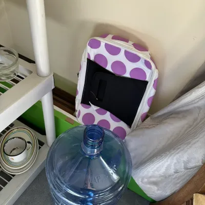 Sale Photo Thumbnail #666: Large blue plastic 5-gallon water jug resting on the floor beside a purple polka-dot tote bag.