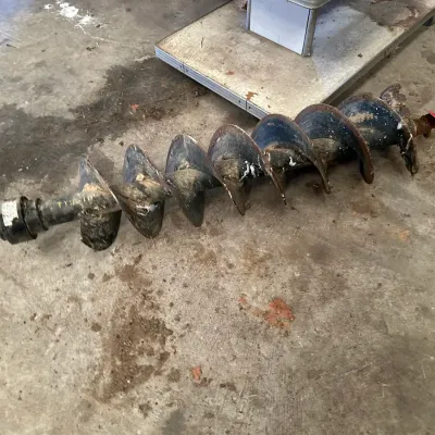 Sale Photo Thumbnail #208: Heavy-duty steel auger bit attachment for post hole digging, showing signs of prior use with surface dirt and light wear.