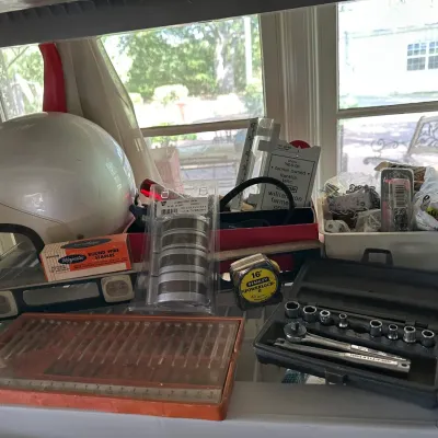 Sale Photo Thumbnail #656: Assorted workshop tools and supplies, including a vintage white motorcycle helmet, socket set, Stanley Powerlock tape measure, and drill bit set.