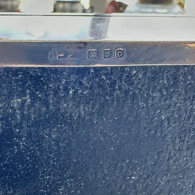 Sale Photo Thumbnail #397: Detail shot showing English sterling silver hallmarks stamped into the metal rim of an item mounted on a textured blue base.